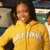 A person in a yellow jacket with white text on the chest, standing against an indistinct background.