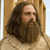 Pixelated portrait of a person with long dark hair and a full beard, wearing a light-colored shirt against a wooden background.