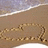 Pixelated beach scene with light brown sand, white wave crest, and muted blue-gray sky, showing partial wave motion and scattered darker sand patches.