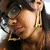 A woman with long dark hair wears large round glasses and gold triangular earrings, her head slightly tilted in a close-up portrait.
