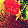 A person in green pants and red high heels holds a red umbrella with white lines on a brick-paved ground.