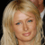 Pixelated close-up of a person with long blonde hair, blue eyes, and a neutral expression against a dark background.