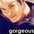 Pixelated close-up of a smiling person with light skin and dark hair, wearing a dark blue top, with the word 'gorgeous' in white block letters at the bottom.