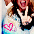 A person with long brown hair wearing a white top makes a peace sign, has an open mouth expression, and displays a pink heart outline on the left side of the image.