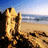 Pixelated beach scene with golden sand, dark rocks, blue sky, and ocean horizon under bright sunlight.