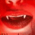A close-up of a red-toned face with dark lips, showing teeth and dripping liquid against a gradient background.