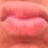A close-up of lips with a soft pink and red gradient, rendered in pixelated style against a blurred background.