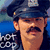 A pixelated image of a man in a police uniform with a mustache, wearing a cap and dark jacket against a blue background.