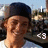 A person wearing a dark cap and white shirt smiles in a pixelated outdoor scene with text overlays.
