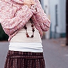 A person wearing a pink floral-patterned long-sleeve top, white undershirt, and brown plaid skirt with a beaded necklace visible.
