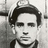 Black-and-white photograph of a person with dark hair and a cap, set against red background with pixelated text.