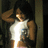 Pixelated figure in white sleeveless top with blue graphic, dark hair, hand raised near head against dim background.