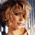 Pixelated close-up of a person with curly brown hair, light skin, and a neutral expression, wearing a light-colored top against a blurred background.