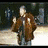 Animated sequence showing a figure in brown robe with white accents, transitioning from outdoor setting to indoor room while holding hands near chest.