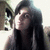 Pixelated static image of a person with long dark hair wearing a dark top, positioned against a light background with a blurred figure on the left.