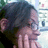 A person with dark hair and glasses covers their mouth with both hands in a pixelated image with a blurred background.