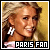 Pixelated image of a person with light brown hair styled in an updo, wearing large white earrings and pink clothing against a yellow background.