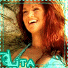 A static pixelated image of a person with long red hair wearing a light blue top, smiling with eyes closed against a blurred background.