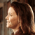 Pixelated profile view of a person with brown hair tied back, wearing a dark top against a blurred background.