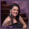 A woman in a black strapless dress sits in a theater-like setting with purple walls and brown seats, smiling and shifting her head position across frames.