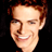 Pixelated static image of a smiling person with light brown hair against black background, rendered in low-resolution 256x256 pixels.