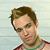 Static pixelated image of a person with brown hair wearing sunglasses and a green necklace against a light background.