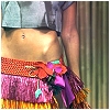 A cropped image shows a person's midsection with a belly button piercing, wearing a red patterned belt and a purple skirt with a turquoise pendant.