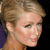 Pixelated close-up of a person with light brown hair styled in an updo, showing side profile with closed eyes and neutral expression against dark background.