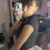 Pixelated static image of a person with light skin holding a silver digital camera, wearing dark clothing against a blurred background.