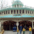 Static image of a building facade with columns, arched windows, and people in front; teal dome on top.