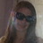 Pixelated image of a person with dark hair wearing sunglasses, holding an object near their face against a gradient background.
