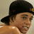 Pixelated image of a person wearing a black cap with red and yellow details, shirtless torso visible against light background.