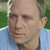Pixelated close-up of a person's face with light skin tone, short brown hair, and a light blue collared shirt against a green background.
