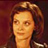 Pixelated static image of a person with light brown hair and warm-toned skin against a dark reddish-brown background.