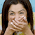 Static 50x50 pixel icon showing a person with long dark hair covering their mouth, wearing a yellow top against a light blue and beige background.