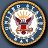 Circular emblem with golden border, blue field of white stars, central bald eagle holding arrows and olive branch, red shield on chest, orange crown above head.