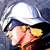 Pixelated image of a person wearing a white hard hat and dark blue jacket, with visible hands holding an object against a blurred background.