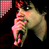 A person holding a microphone near their mouth, with a red and white pixelated heart pattern in the top-left corner, displayed in a of