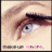 Close-up of a light-skinned person's eye with brown eyelashes and eyebrow, blue iris, visible skin texture, and pixelated lower text elements.