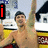 A person with dark hair and a cap raises both arms in victory, wearing red swim trunks against a blurred background.
