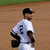 A baseball player in a white uniform with number 3 on the back walks across a dirt field, viewed from behind.