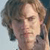 Pixelated static image of a person's face with light brown hair and neutral expression against blurred background.
