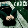 A person lies on a wooden surface with hands clasped over their chest, wearing dark clothing and a blue top, with text above reading "AS IF YOU EVER CARED".
