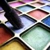 A close-up of a makeup palette with multiple colored eyeshadow pans and a black makeup brush resting on the palette.