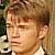Pixelated close-up of a person with light brown hair, wearing a white shirt against a blurred background.