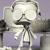 Pixelated grayscale image of a figure with large rounded head, dark facial features, and outstretched arms against purple background.