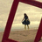 A pixelated figure in a dark dress stands on a beach under a light sky, framed by deep red borders.