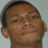 Pixelated close-up of a person's face with short dark hair, light brown skin, and a neutral expression against a light gray background.