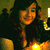 A woman with long dark hair and a sleeveless top smiles at the camera in warm lighting.