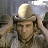 Pixelated image of a person wearing a light-colored helmet with a dark brim, standing against a blurred background with muted tones.